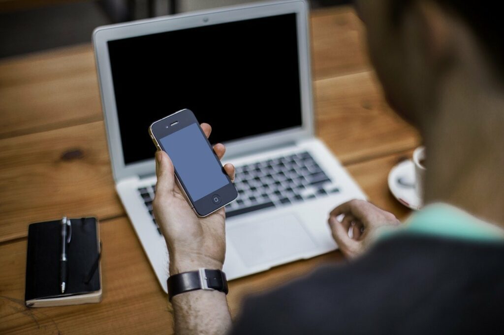 Contact us - man in front of laptop at table holding his cell phone